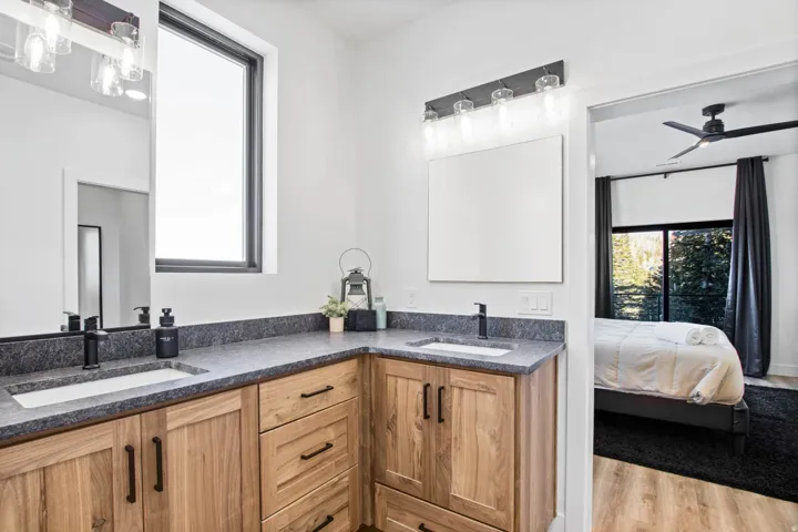Dual vanity with under-mount sinks, dark stone countertops, and wood-finish cabinetry