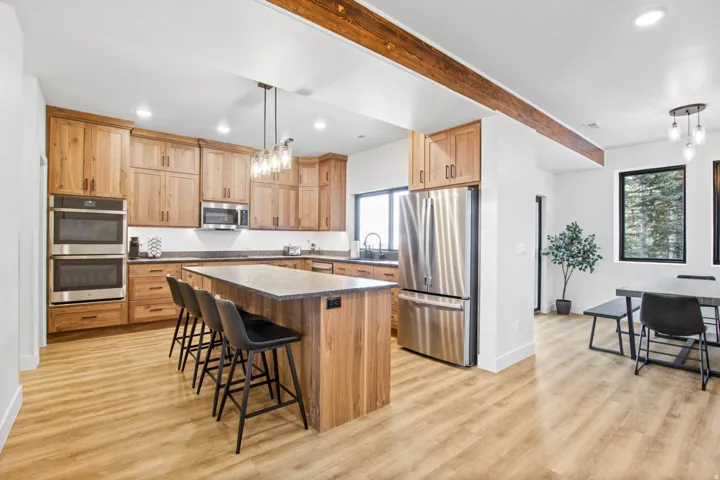 Kitchen featuring wood cabinetry, stainless steel appliances, a center island with seating, pendant lighting, and wood-finish flooring