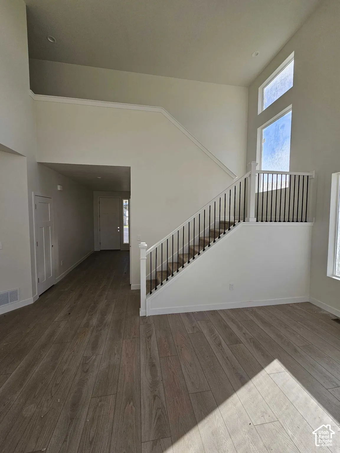 Two-story foyer with high ceilings, wood-finish flooring, and a staircase featuring black metal spindles and white risers