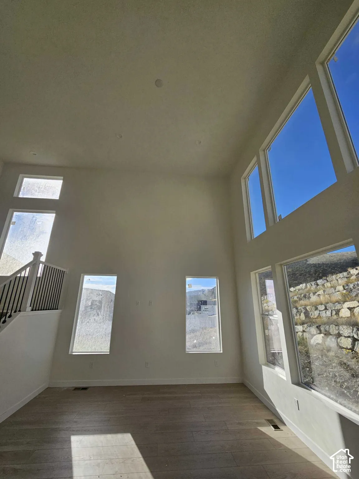 Expansive living area with high ceilings, recessed lighting, wood-finish flooring, and multiple large windows