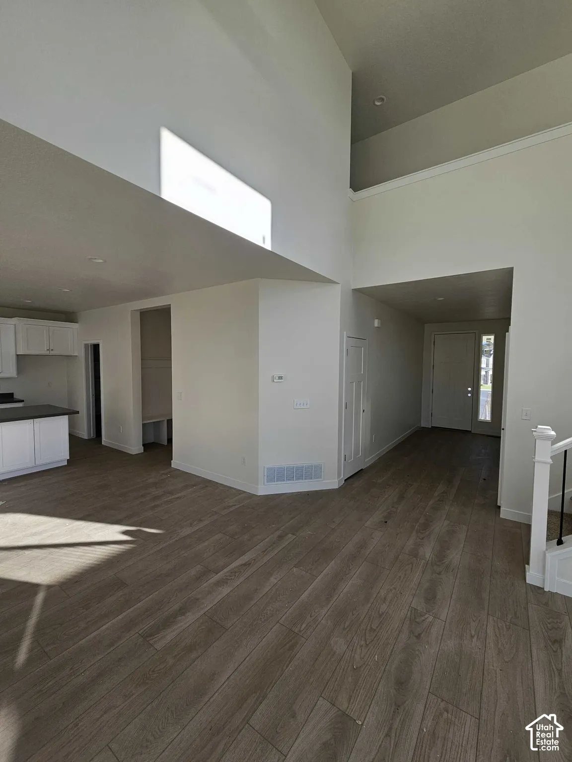 Vaulted ceiling with an upper window, wood-finish flooring, white cabinetry, and white staircase with black iron balusters