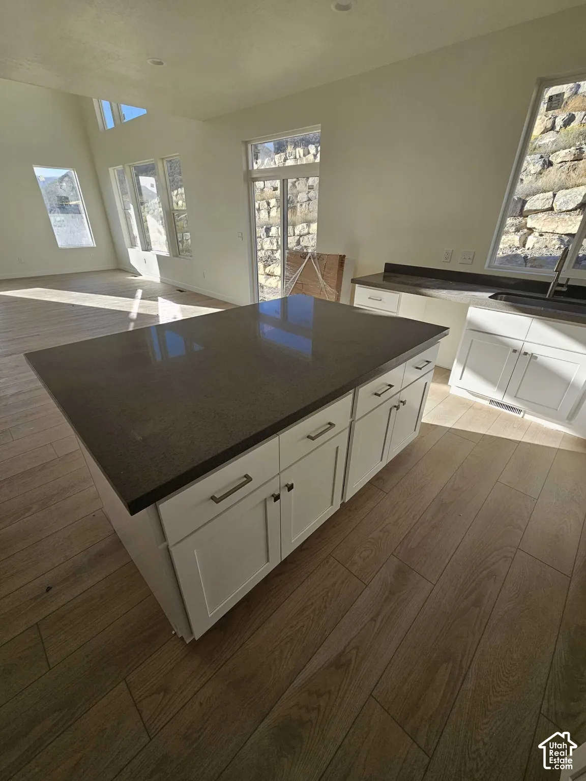 Kitchen island with a dark countertop and white cabinetry, wood-finish flooring, and recessed lighting