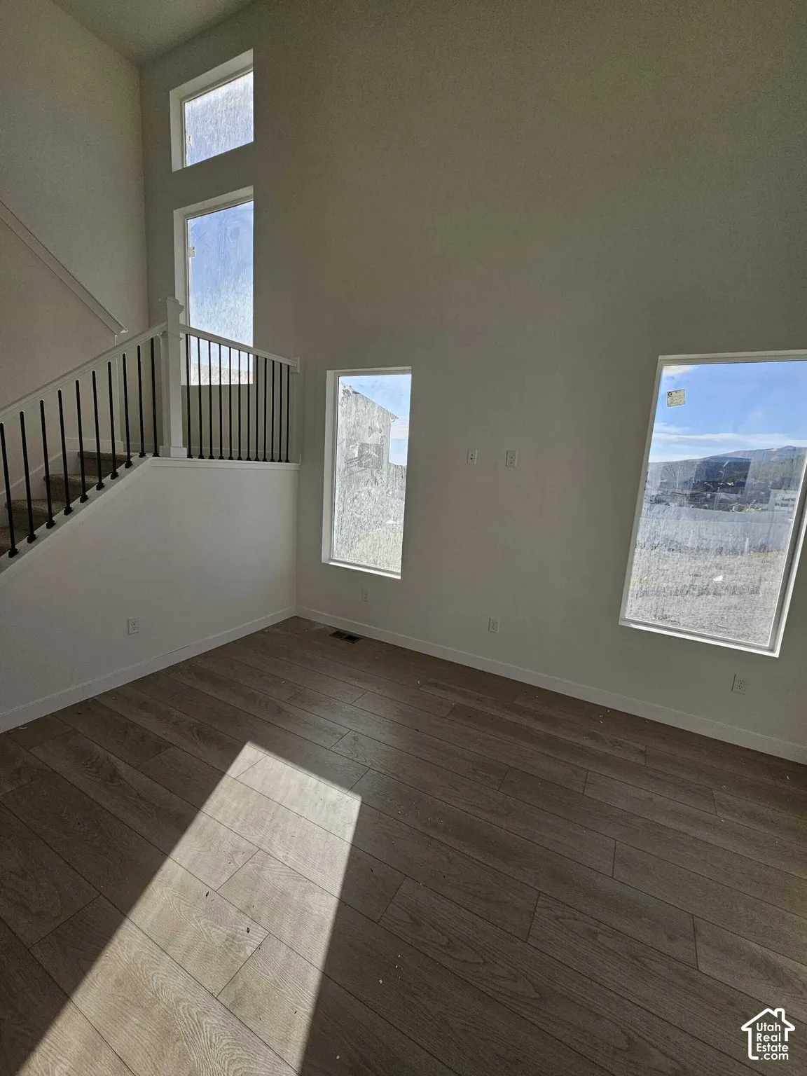 Vaulted ceiling with multiple windows, wood-finish flooring, and a staircase featuring a black wrought iron railing