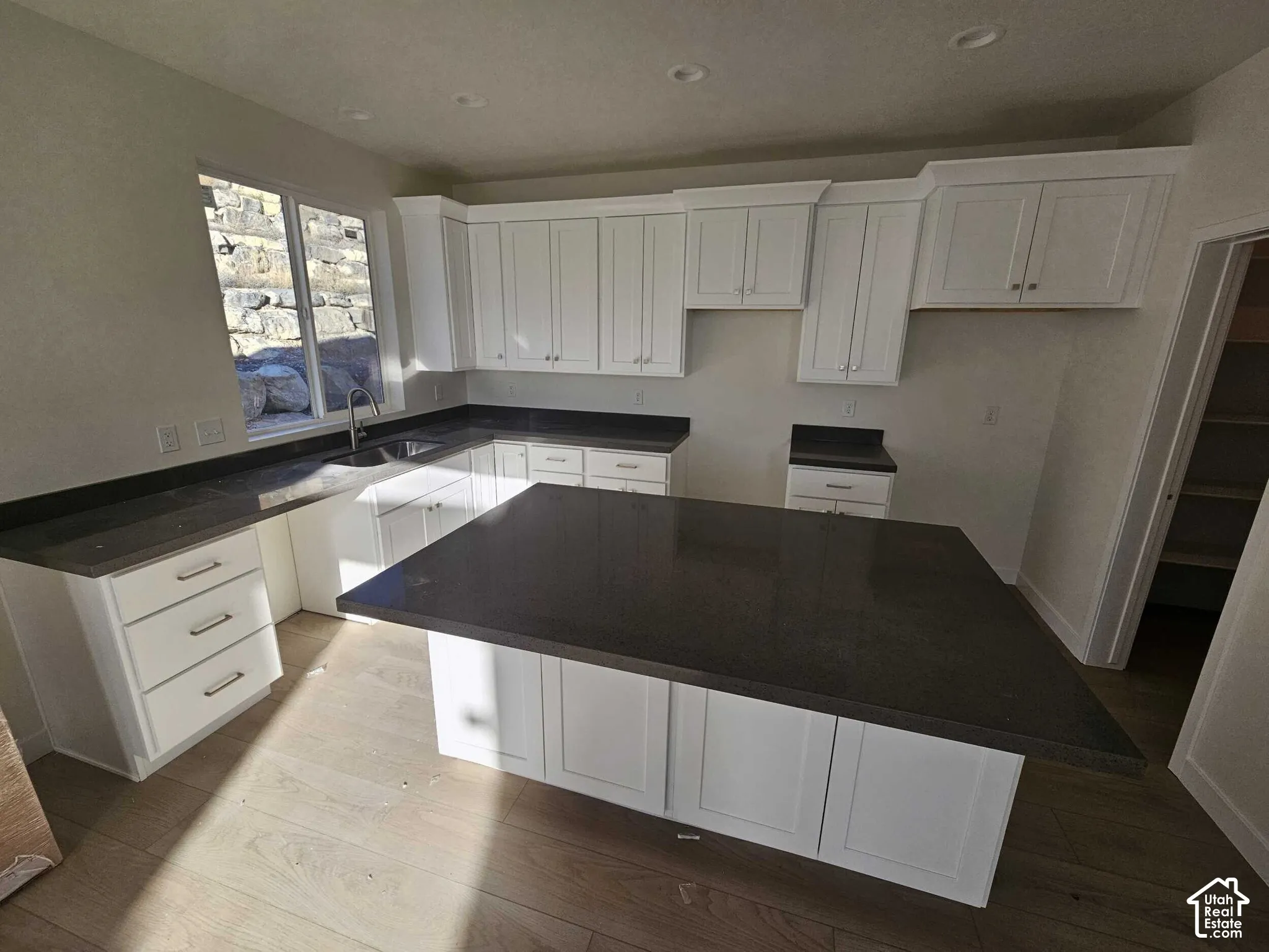 Contemporary kitchen featuring an expansive island, white cabinetry, dark countertops, wood-finish flooring, and recessed lighting