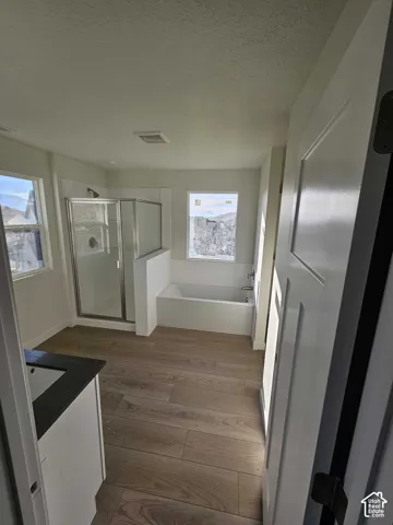 Wood-finish flooring, built-in bathtub, glass-enclosed shower, dual windows, and a vanity with a dark countertop