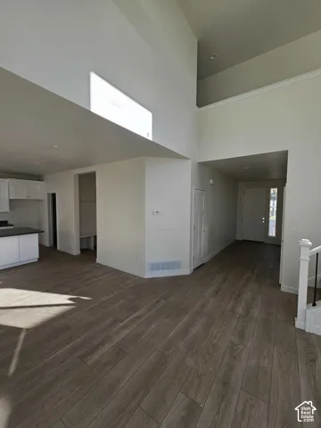 Vaulted ceiling with an upper window, wood-finish flooring, white cabinetry, and white staircase with black iron balusters