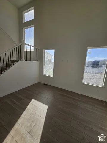 Vaulted ceiling with multiple windows, wood-finish flooring, and a staircase featuring a black wrought iron railing