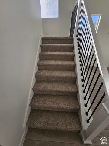 Carpeted staircase featuring a contemporary metal spindle railing, white newel posts, and natural light from transom windows