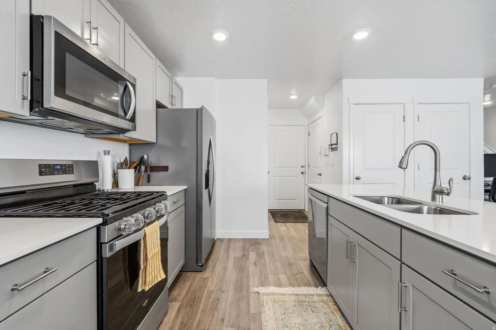 Modern kitchen featuring stainless steel appliances, light gray cabinetry, white countertops, a double-basin sink with a pull-down faucet, and wood-finish flooring