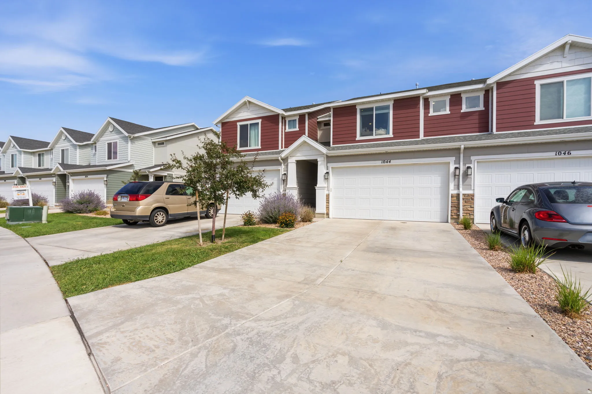 Townhome exterior with a red and white facade, featuring an attached garage, concrete driveway, and rock landscaping