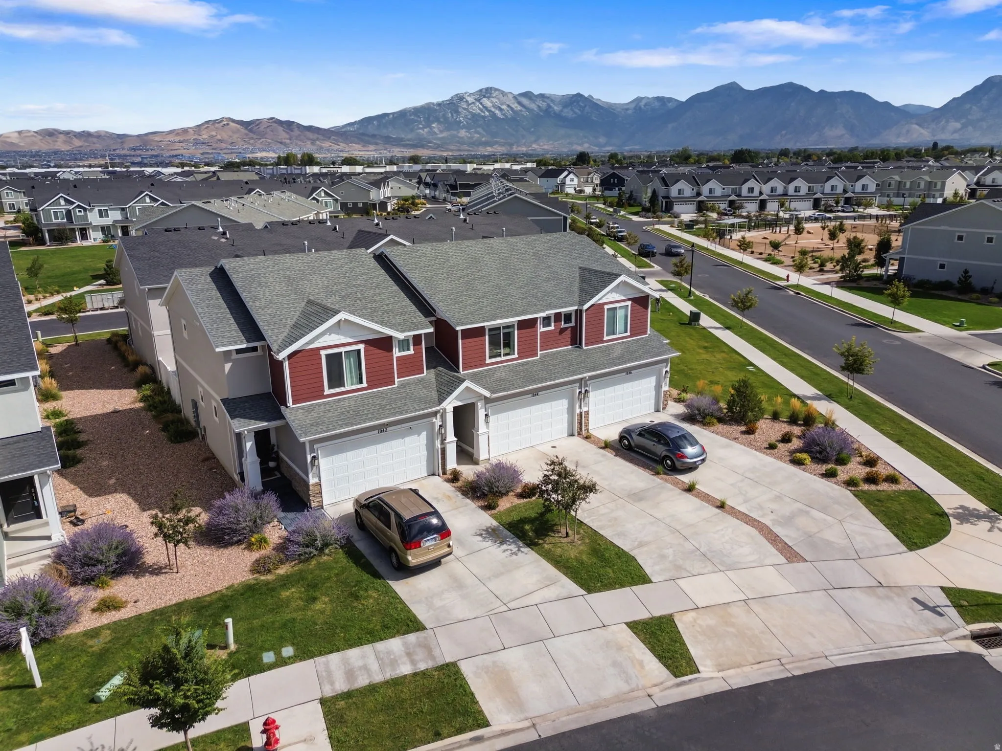 Two-story duplex with a red and beige exterior, white garage doors, and concrete driveways