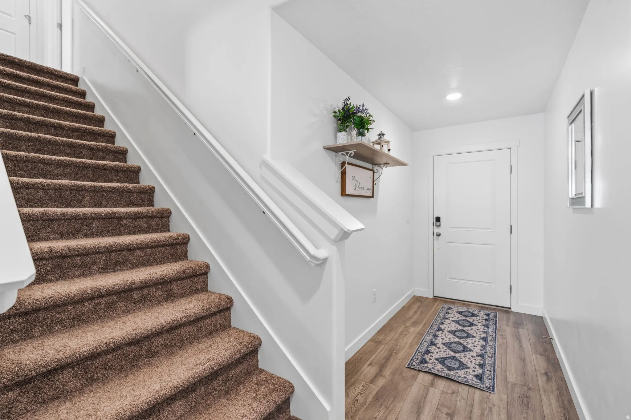 Carpeted staircase with white handrail, recessed lighting, wood-finish flooring, and a paneled entry door