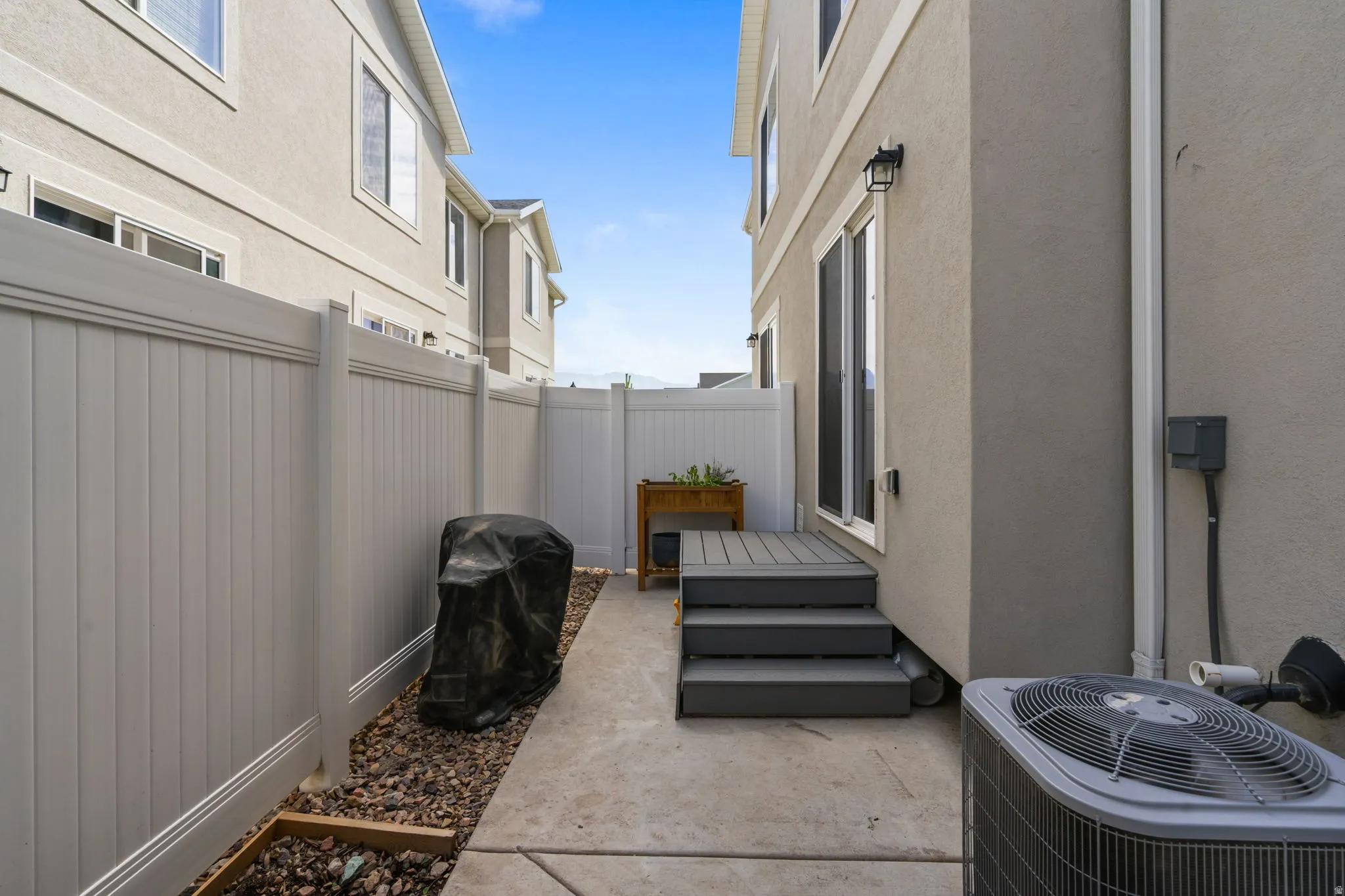 Private fenced outdoor space featuring a concrete pathway, rock landscaping, and a multi-level composite deck