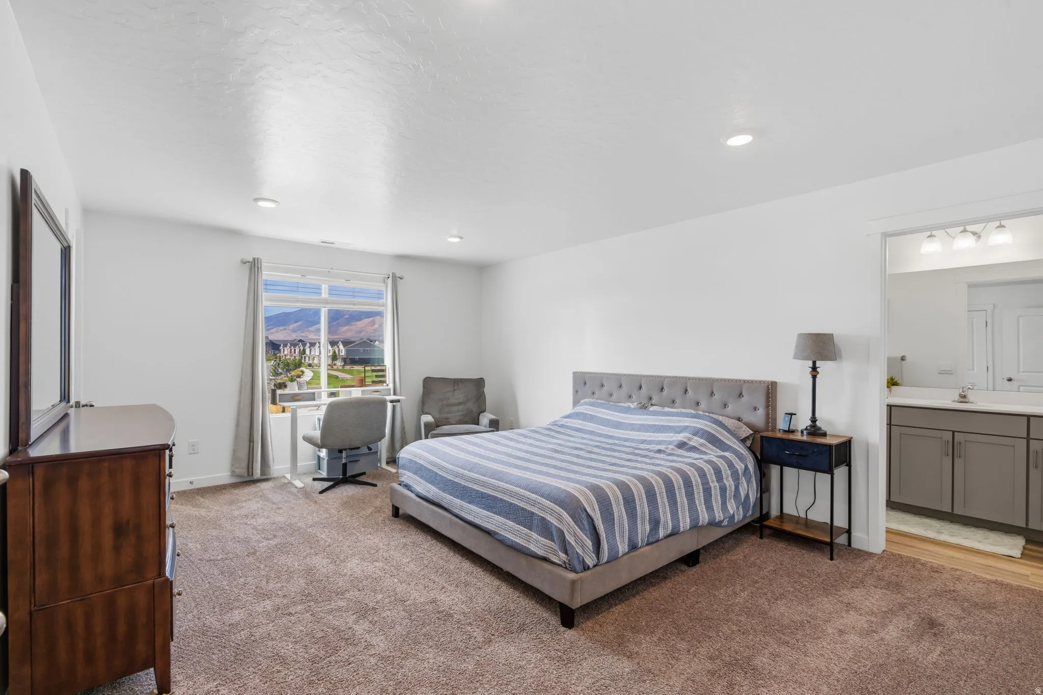 Recessed lighting, large window with mountain scenery, attached bathroom with dual vanity, and wood-finish flooring