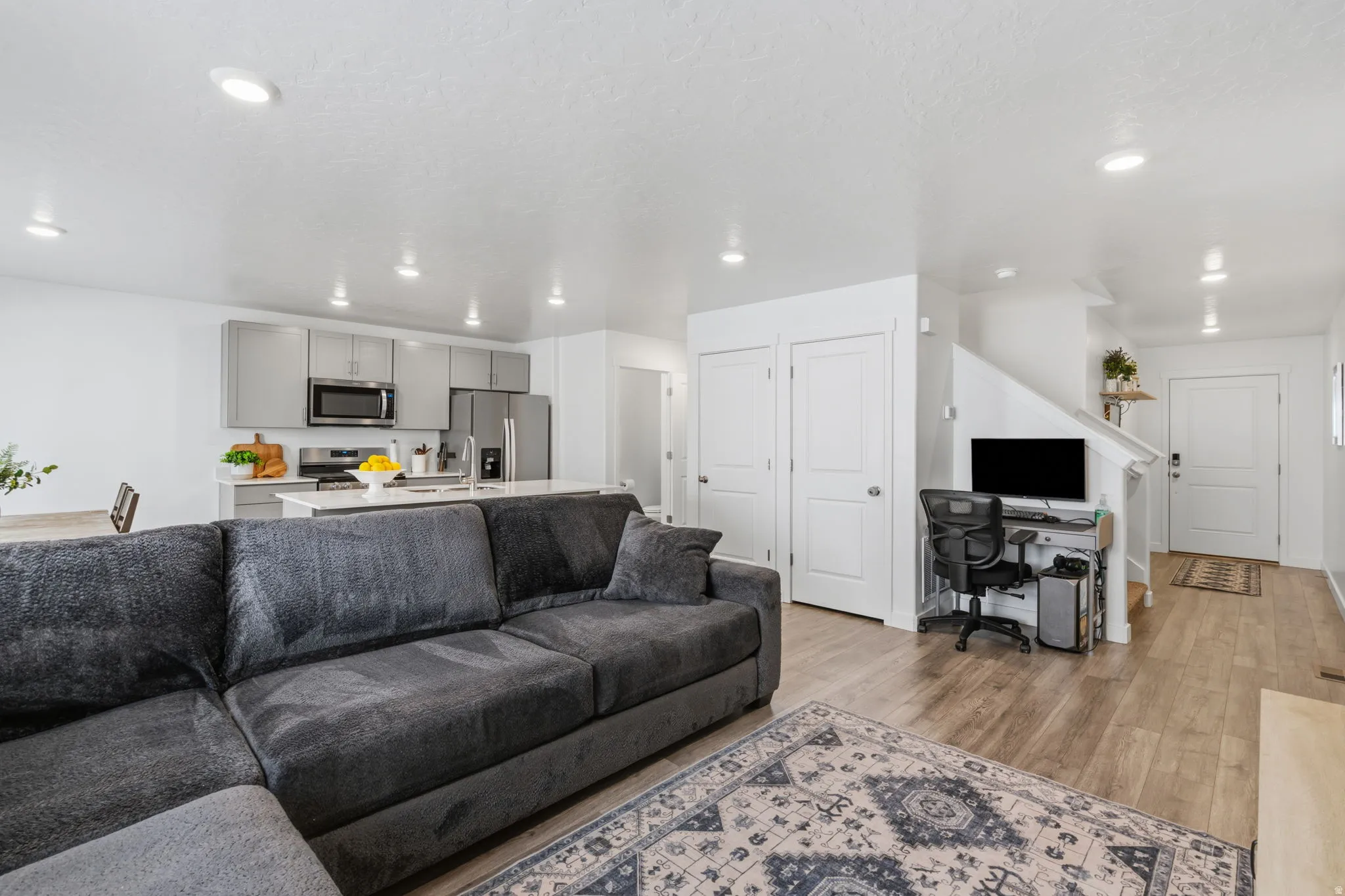 Recessed lighting, wood-finish flooring, white walls, gray kitchen cabinetry, and stainless steel appliances