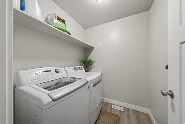Dedicated laundry room featuring side-by-side washer and dryer appliances, floating shelving with storage, wood-finish flooring, and abundant natural lighting from recessed ceiling fixtures