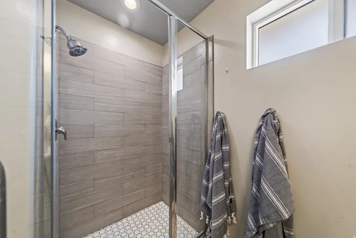Shower enclosure with clear glass doors, wood-finish tile walls, and white hexagonal tile flooring