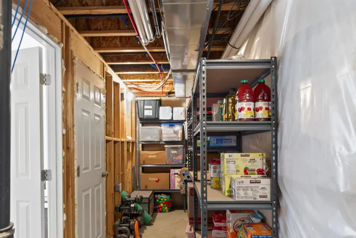 Unfinished basement featuring exposed wood framing, white paneled doors, exposed ceiling joists, and a metal shelving unit