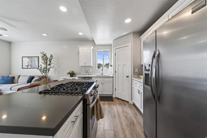 Gourmet kitchen with stainless steel appliances, white cabinetry, dark countertops, and wood-finish flooring