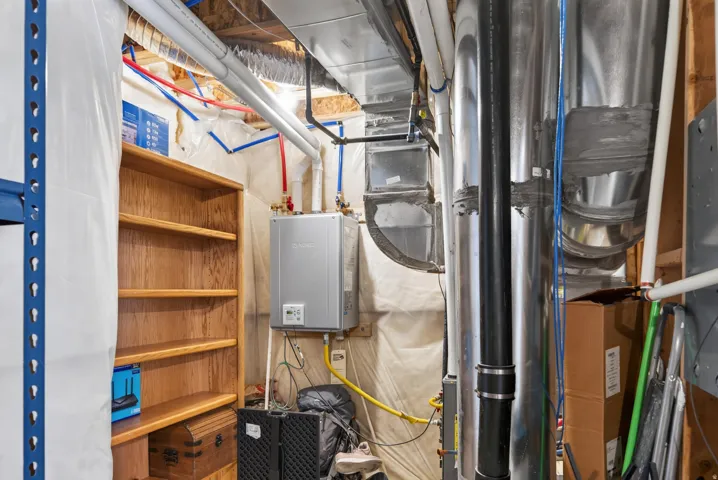 Wall-mounted water heater with exposed utility lines and ceiling ductwork