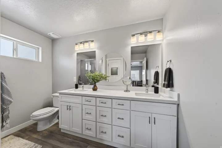 Dual vanity with white cabinetry and integrated sinks, wood-finish flooring, and horizontal window
