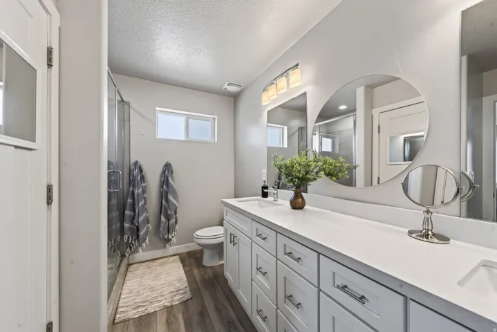 Master bathroom. Extended dual vanity with integrated sinks, glass-enclosed shower, wood-finish flooring, and upper window