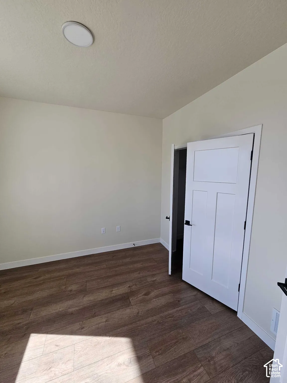 Wood-finish flooring with light-toned walls, a white paneled door, and an overhead flush-mount light fixture