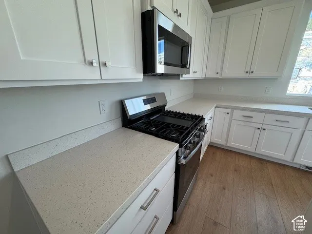 White shaker-style cabinetry with brushed nickel hardware, stainless steel gas range, built-in microwave, and wood-finish flooring