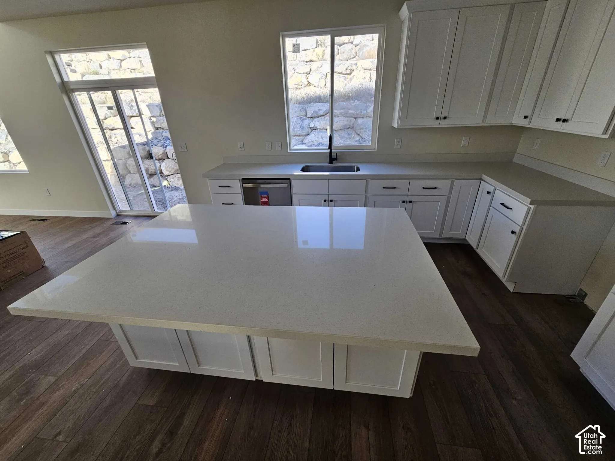White cabinetry with dark hardware, a large kitchen island with a light-toned countertop, a built-in dishwasher, and wood-finish flooring