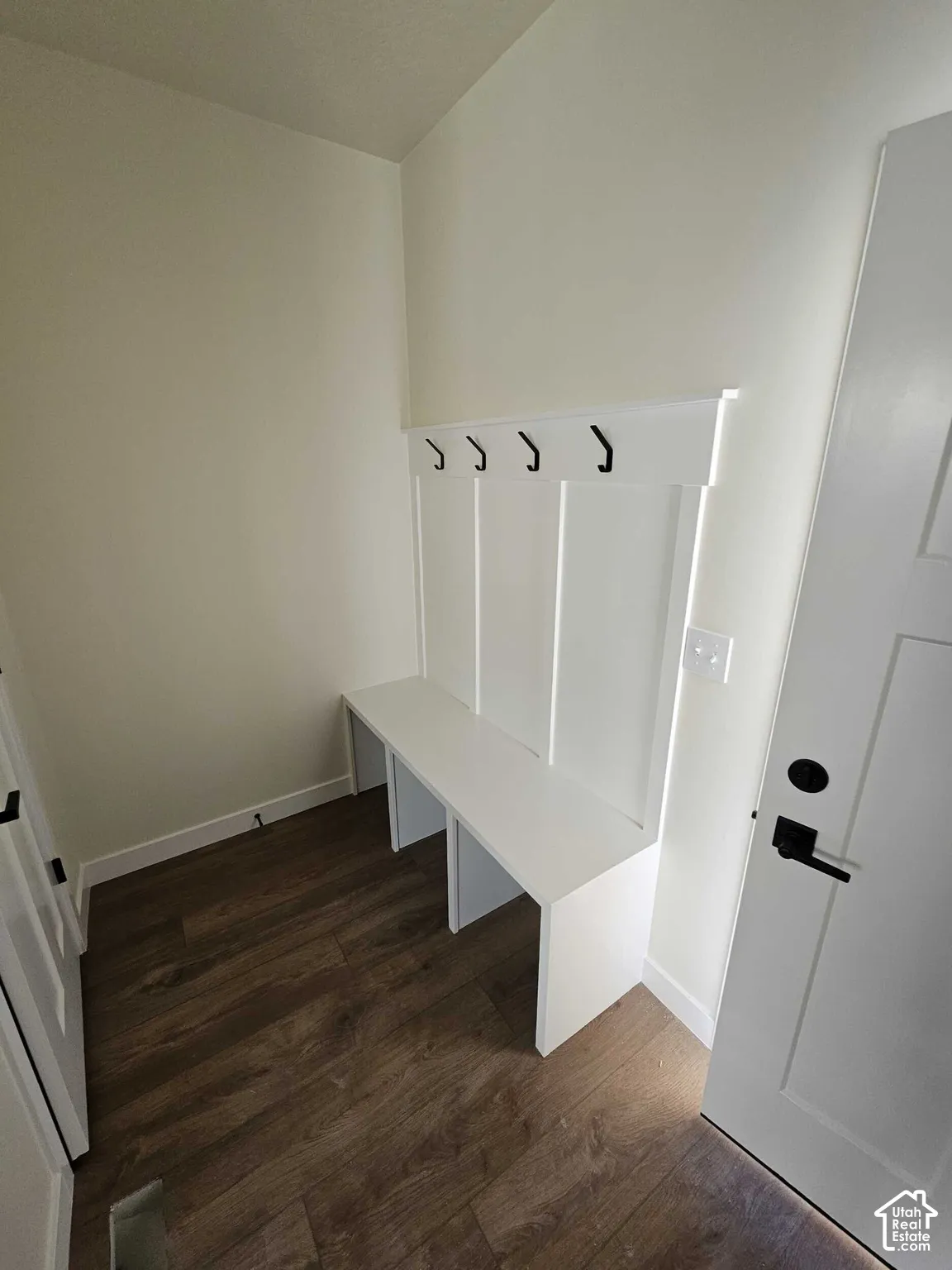 Built-in bench with integrated wall paneling, black coat hooks, and wood-finish flooring