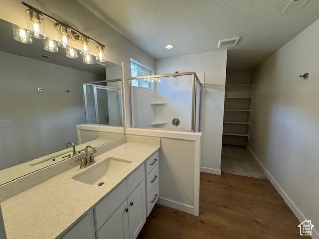 Wood-finish flooring, quartz-finish vanity with integrated sink, glass-enclosed shower, built-in shelving, and contemporary vanity lighting