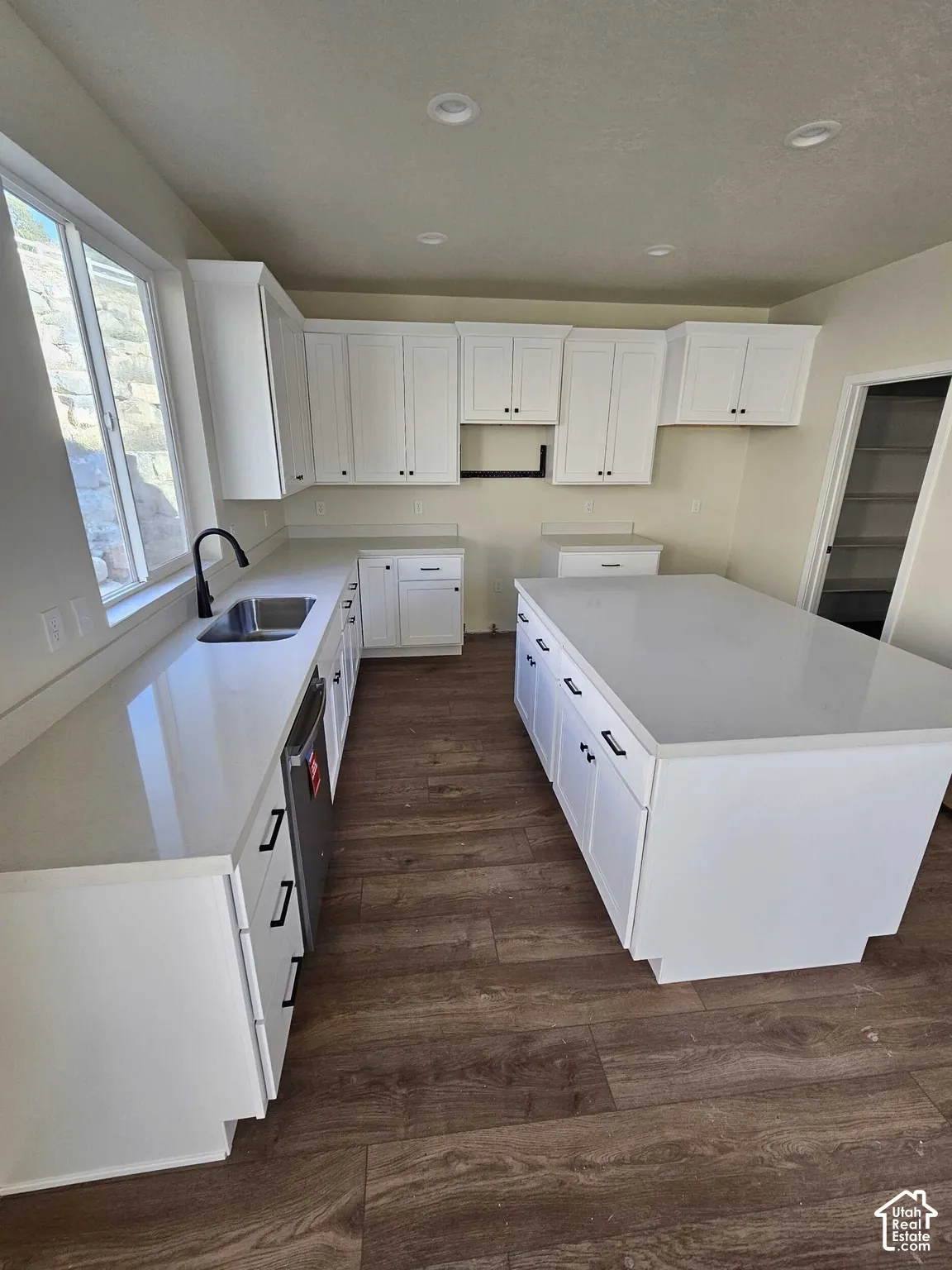 Kitchen featuring white shaker cabinetry, an expansive center island, integrated dishwasher, a stainless steel sink with a matte black faucet, and wood-finish flooring