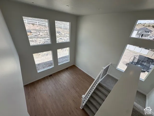 Two-story interior with wood-finish flooring, a carpeted staircase with white newel posts and black iron balusters, and multiple pane windows