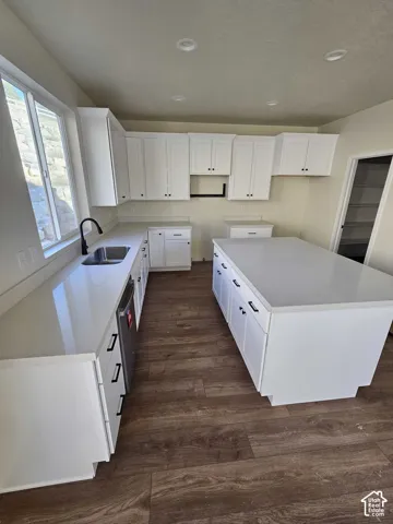 Kitchen featuring white shaker cabinetry, an expansive center island, integrated dishwasher, a stainless steel sink with a matte black faucet, and wood-finish flooring