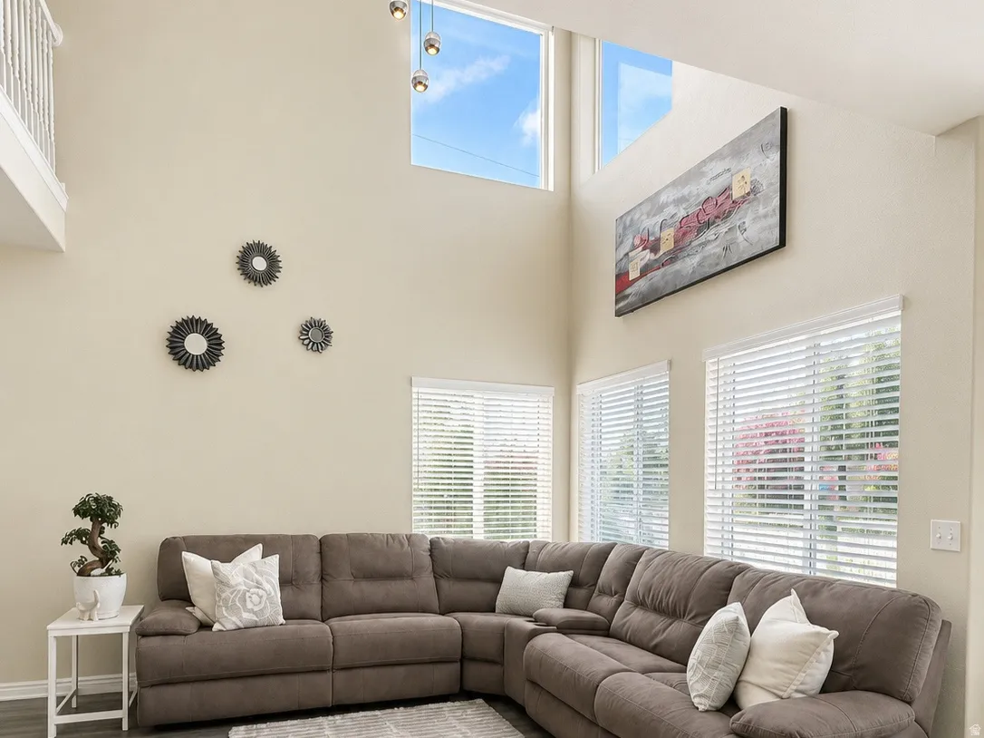 Volume ceiling with upper transom windows, multiple windows with blinds, wood-finish flooring, and white painted walls