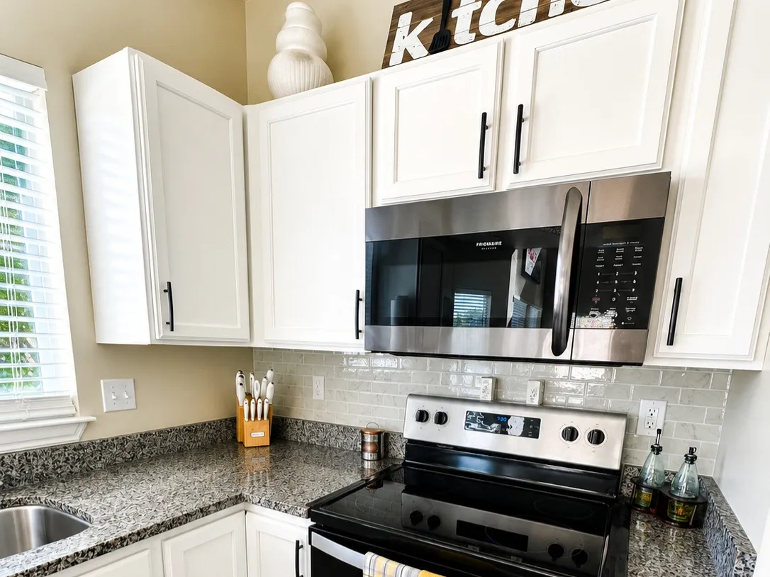 White cabinetry with black hardware, granite-style countertops, stainless steel microwave, glass cooktop range, and wood-finish flooring