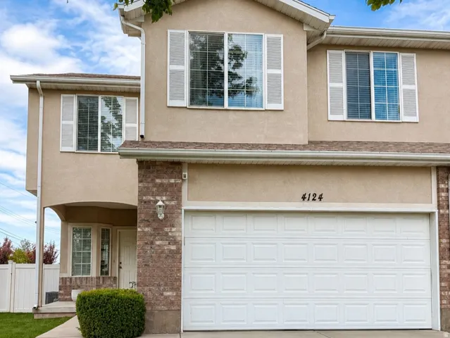 Two-story stucco facade featuring white shutters, a brick accent wall, and a two-car garage with a concrete driveway