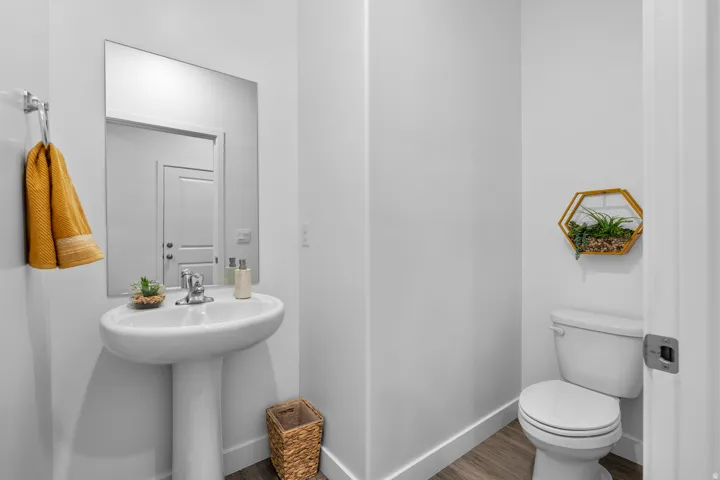 Pedestal sink with chrome faucet, wall-mounted mirror, white toilet, and wood-finish flooring
