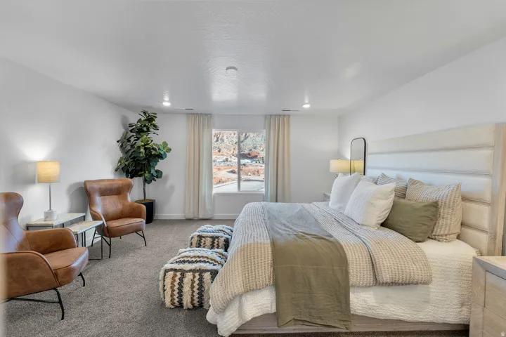 Recessed lighting, window with exterior scenery, carpet flooring, upholstered headboard, and a built-in nightstand