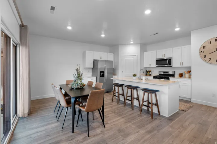Open-concept kitchen and dining area featuring wood-finish flooring, white cabinetry, recessed lighting, and stainless steel appliances