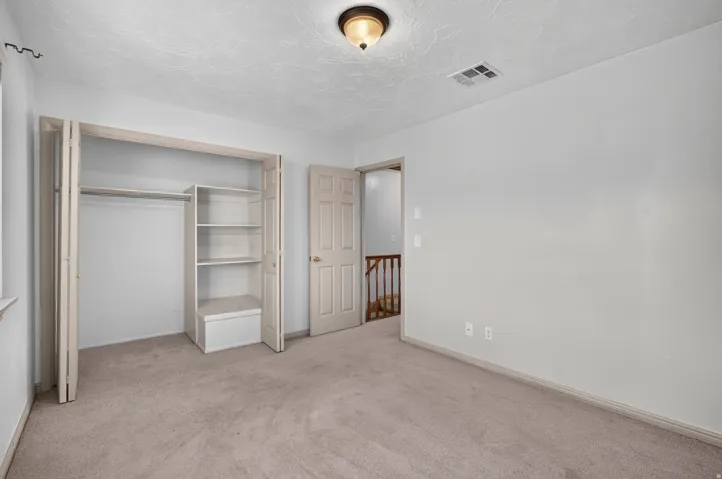 Neutral tone wall paint, carpeted flooring, built-in closet shelving, and a flush mount ceiling light fixture