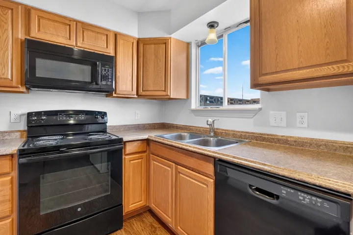 Kitchen featuring wood cabinetry, laminate countertops, a double basin sink, and black appliances including a range, microwave, and dishwasher