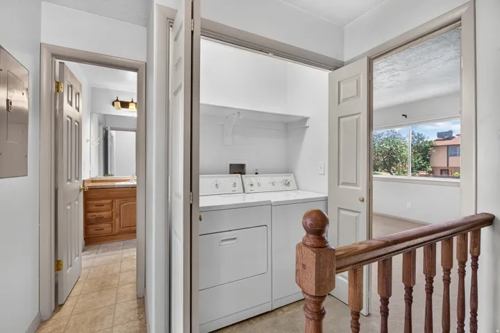 Laundry closet featuring built-in shelving, adjacent to a bathroom with a wood-finish vanity and mirror