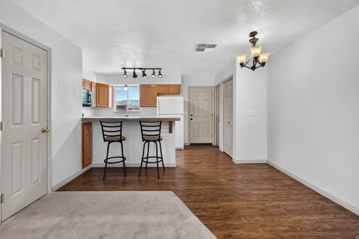 Open-concept living space featuring wood-finish flooring, a kitchen with wood cabinetry and a breakfast bar, and a dining area with a chandelier