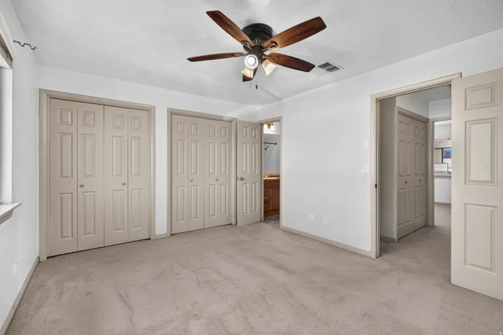 Recessed window, ceiling fan with light fixture, light-toned carpeting, multiple paneled closet doors, and a neutral wall palette