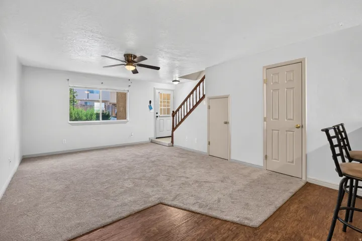 Spacious living area featuring neutral carpeting, a ceiling fan with integrated lighting, and a large window