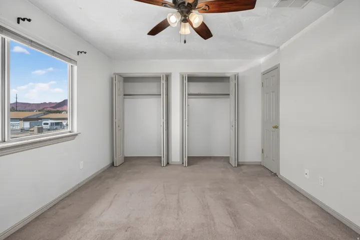 Room featuring two bi-fold door closets, a ceiling fan with light fixture, carpeted flooring, and a window with mountain scenery