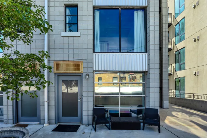 Grey block exterior, full glass paneled entry door, large upper story window, corrugated metal accents, ground-level glass panels