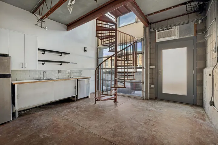 Industrial-style living space featuring exposed ceiling beams, a spiral staircase, and concrete flooring