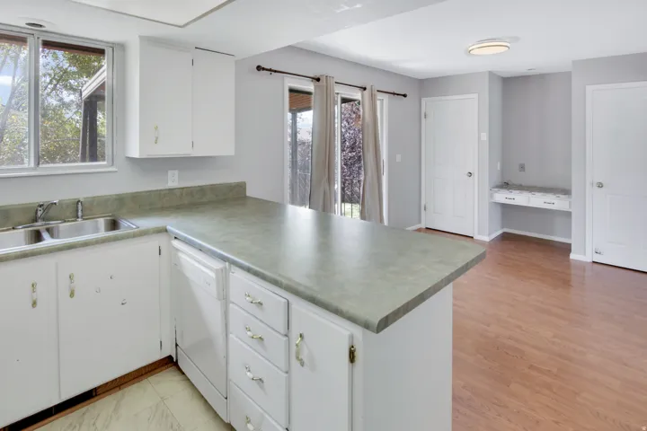Kitchen featuring a double basin sink, white cabinetry, integrated dishwasher, and a built-in desk area